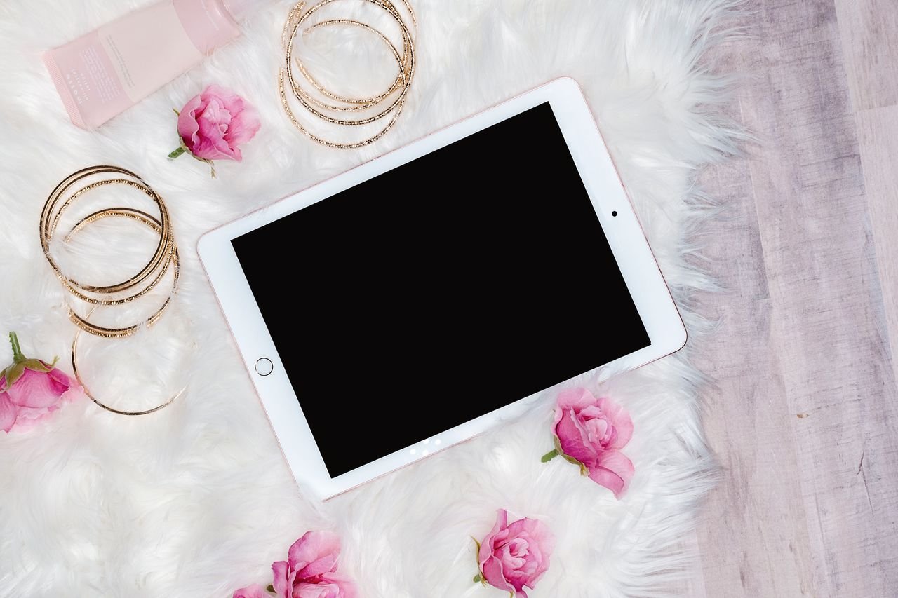 services-04 A stylish flat lay with a tablet, pink roses, and gold bracelets on a soft surface, perfect for product presentation.