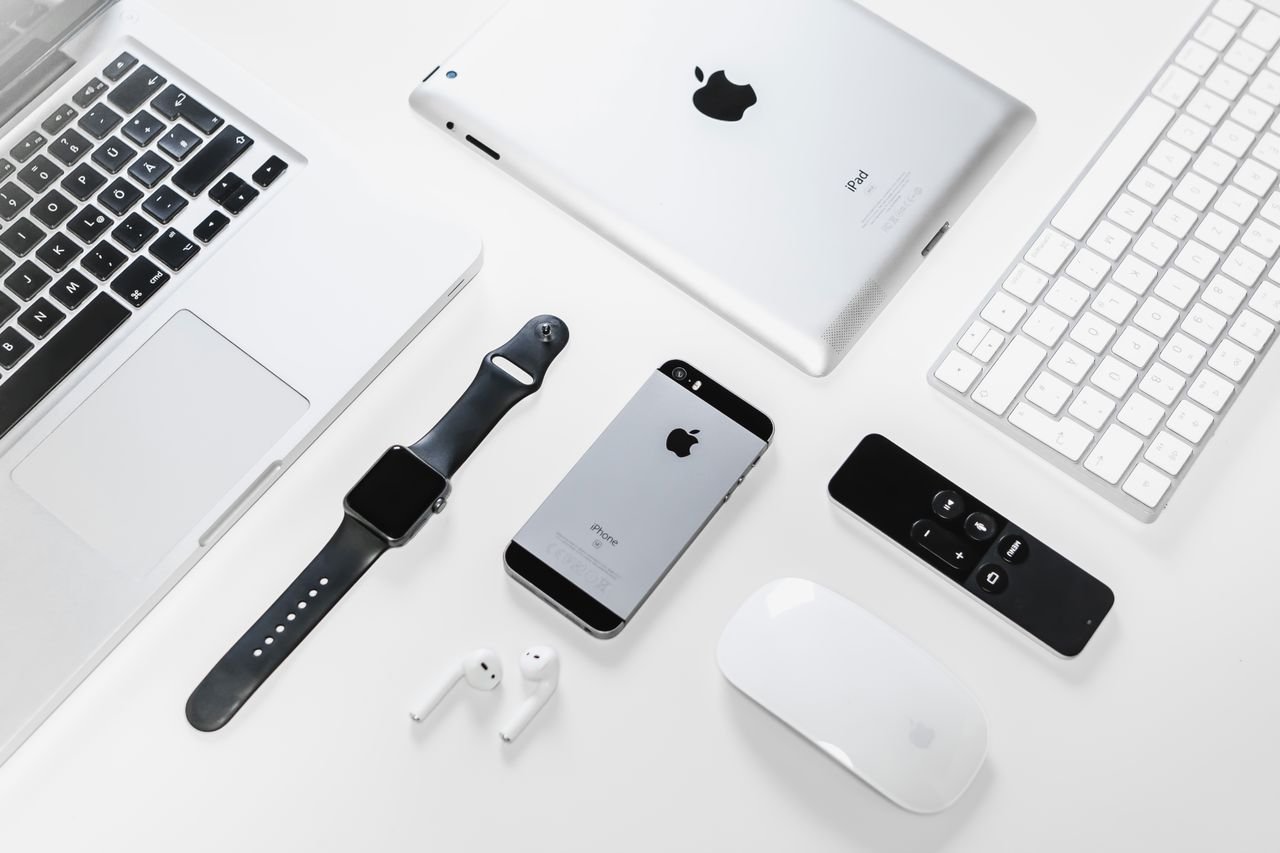 services-01 Flat lay of Apple devices including iPhone, iPad, MacBook, and Watch on a white surface, ideal for tech enthusiasts.