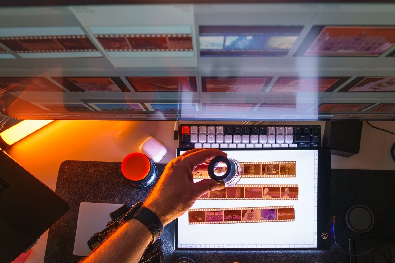 Top view of film negatives being reviewed with a magnifying glass on a light table in a photography darkroom.