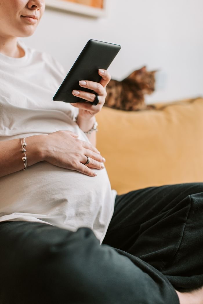 Expectant mother using a tablet on a couch, relaxing at home.